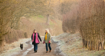 Images of two ladies and a dog taking a walk in the countryside during winter. They are walking along a road with trees on either side