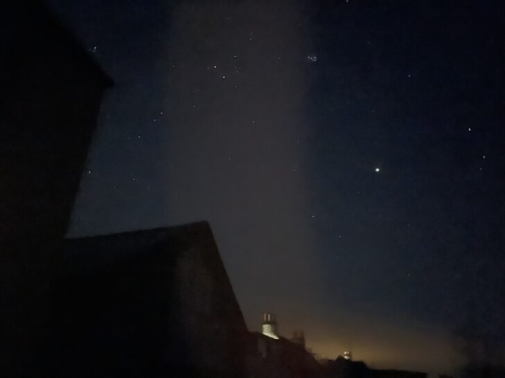 picture showing rooftops and light pollution in bottom of image and the constellation Taurus including The Pleiades in the sky